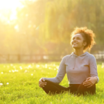 a woman sits cross-legged on grass, the sun is bright behind her