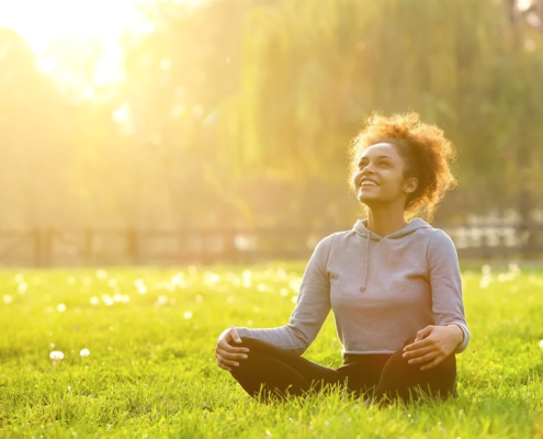 a woman sits cross-legged on grass, the sun is bright behind her