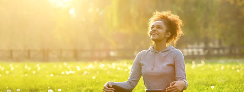 a woman sits cross-legged on grass, the sun is bright behind her