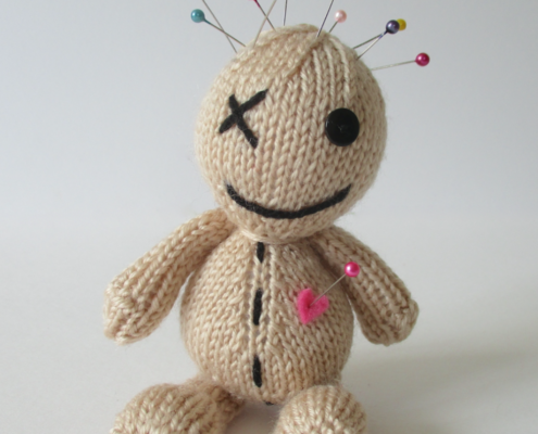 A picture of a cute hand knit voodoo doll, with pins in its head