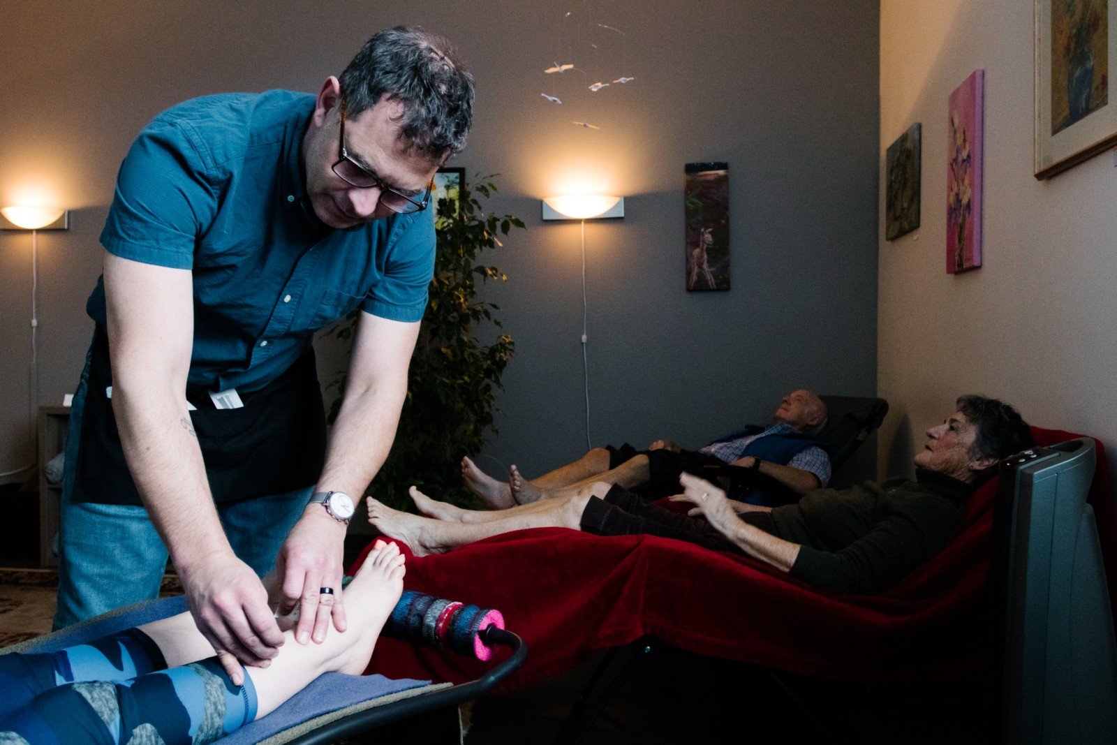 Several people relaxing after receiving acupuncture. Acupuncturist removes needles from a patient in the foreground